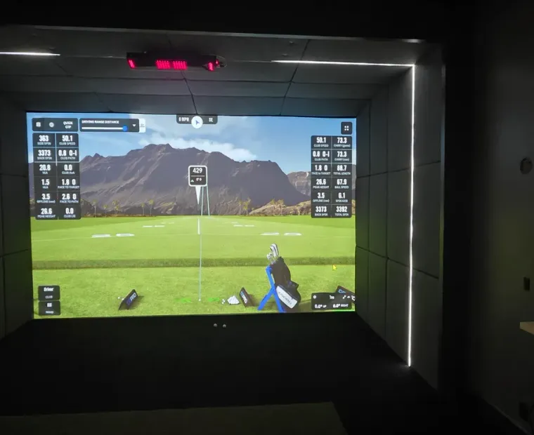 Golfer mid-swing in a Kansas City golf simulator with an overhead launch monitor