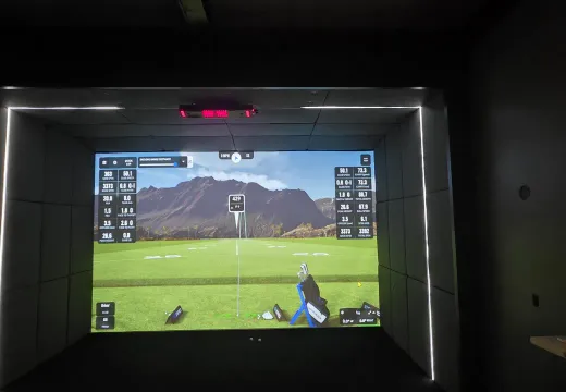 Finished golf simulator bay with an LED-lit screen surround and overhead launch monitor