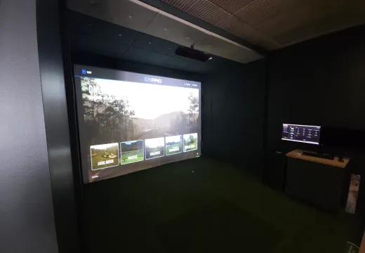 Golf simulator showing the GSPro menu beside a control desk in a finished room