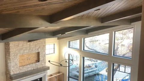 Finished living space with a vaulted wood-beam ceiling, stone fireplace, and lake-view windows