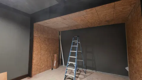 Custom golf simulator room under construction with sheathed walls and a ladder