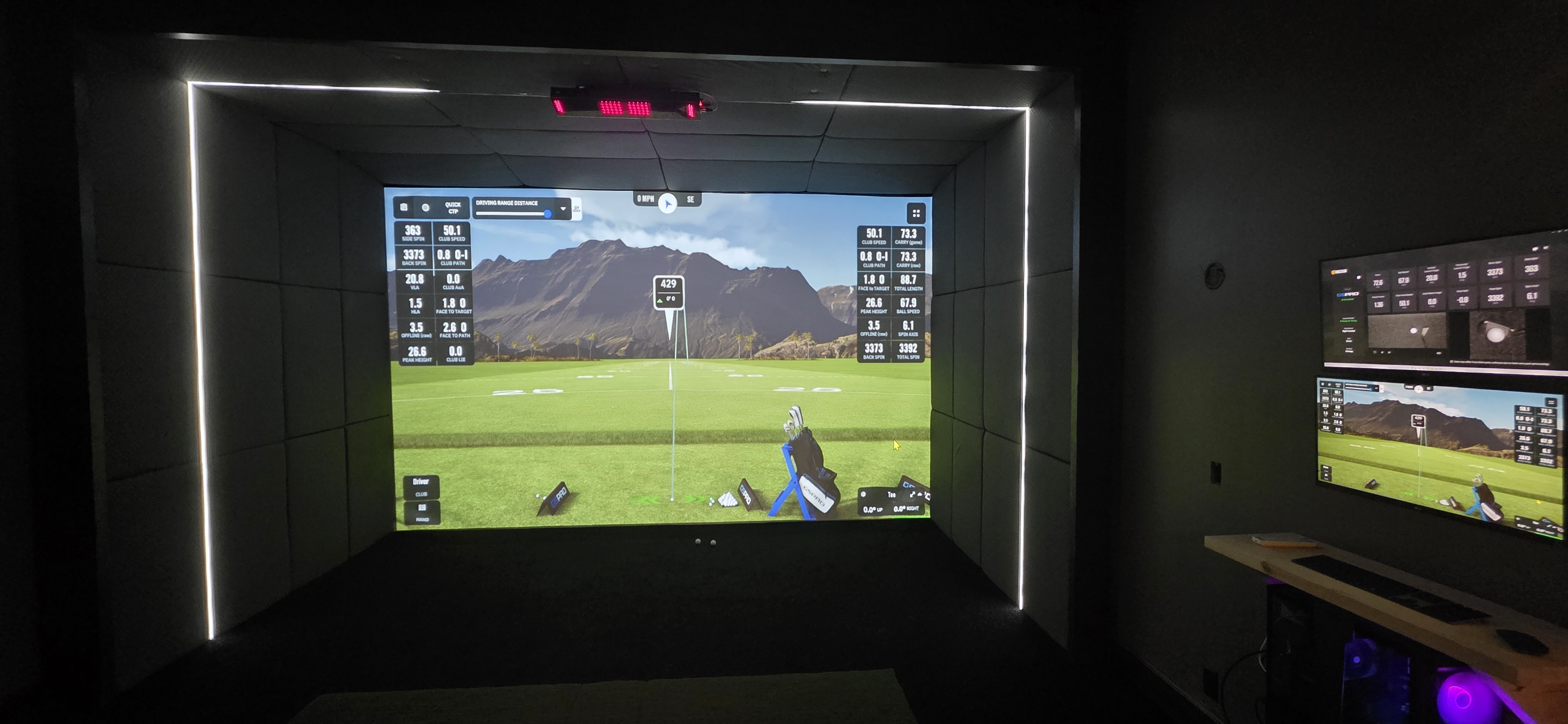 Finished interior of a detached golf simulator building with screen, turf, and even lighting